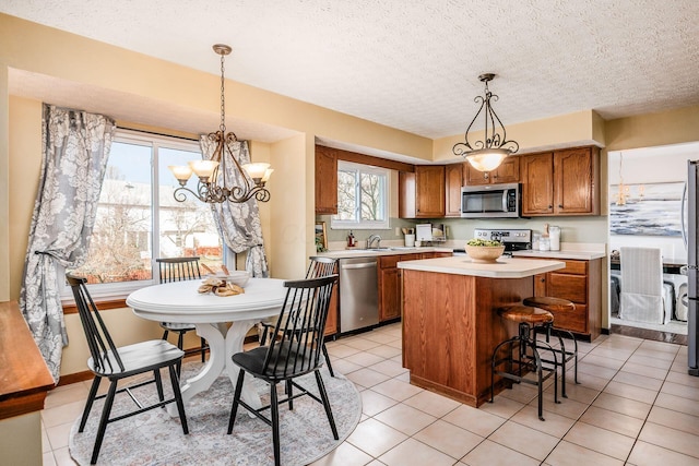 kitchen featuring a sink, a kitchen island, light countertops, appliances with stainless steel finishes, and brown cabinetry