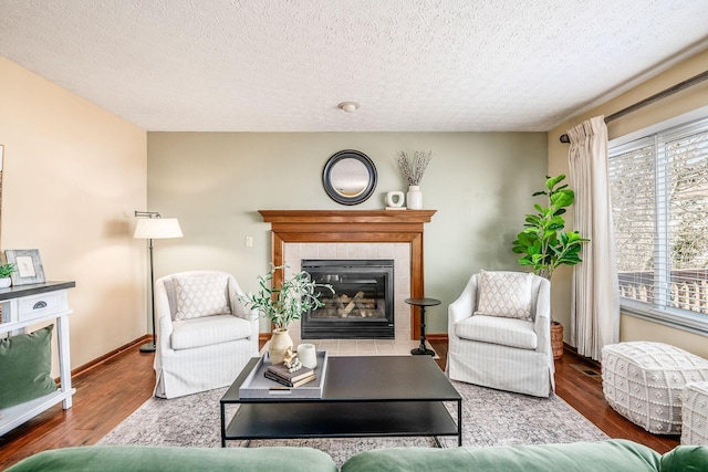 living area featuring a textured ceiling, a fireplace, baseboards, and wood finished floors