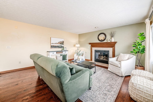 living room featuring a tiled fireplace, a textured ceiling, wood-type flooring, and baseboards