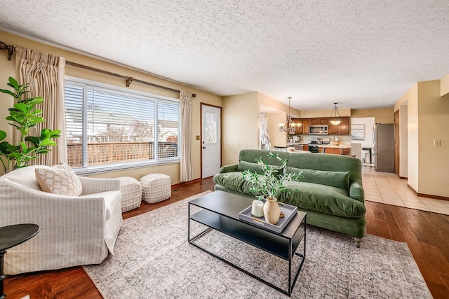 living area featuring a notable chandelier, a textured ceiling, baseboards, and wood finished floors