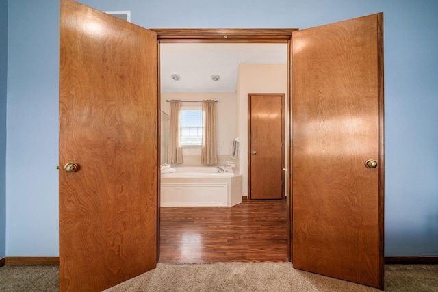 hallway featuring carpet, baseboards, and wood finished floors