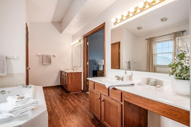 bathroom featuring baseboards, a bath, two vanities, wood finished floors, and a sink