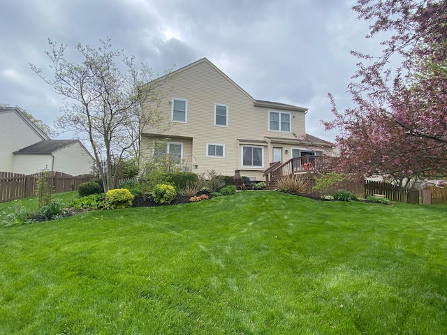 rear view of house featuring a deck, a lawn, and fence