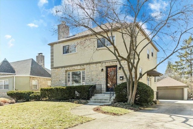 colonial home featuring a front yard, a chimney, stucco siding, an outdoor structure, and a detached garage