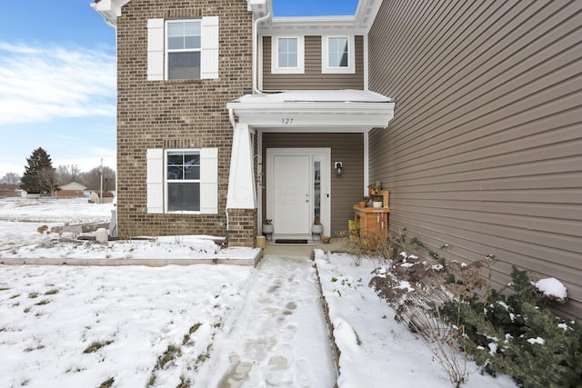 snow covered property entrance featuring brick siding