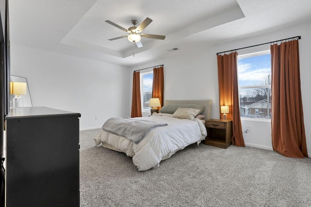 bedroom with light colored carpet, a tray ceiling, multiple windows, and baseboards