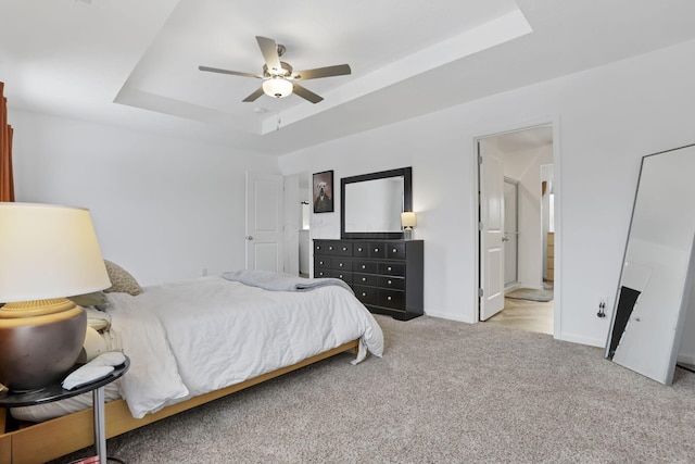 bedroom featuring a tray ceiling, light colored carpet, connected bathroom, ceiling fan, and baseboards