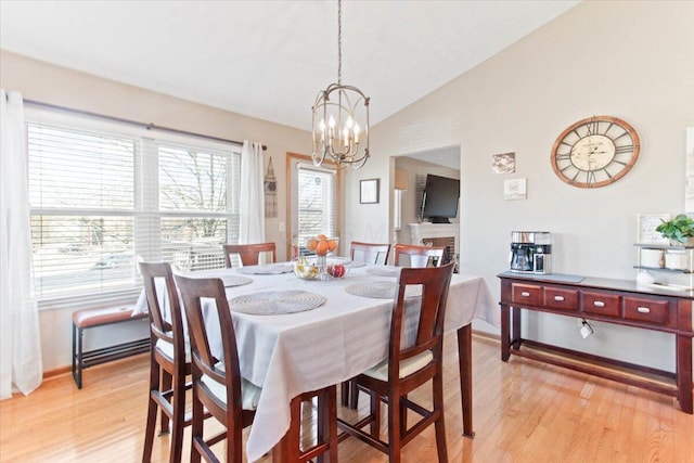 dining room with baseboards, vaulted ceiling, light wood-style floors, a fireplace, and a chandelier