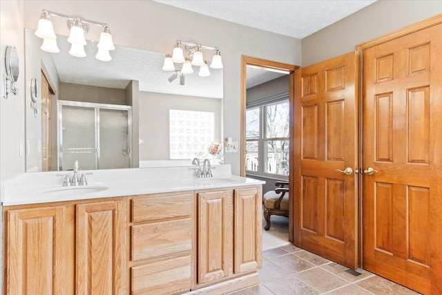 full bathroom featuring a sink, a shower stall, a textured ceiling, and double vanity