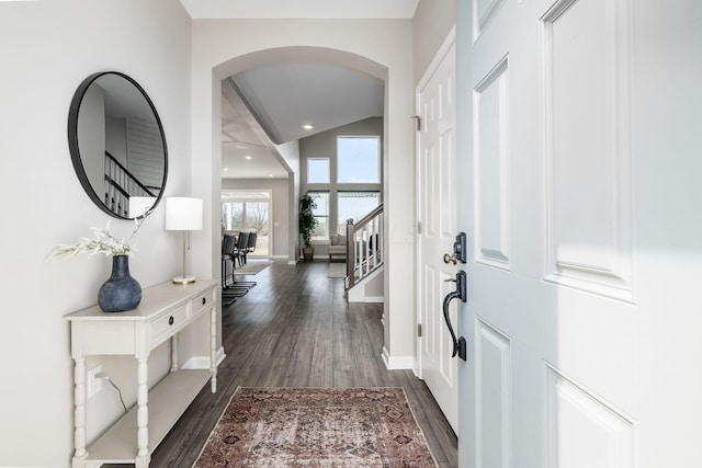 entryway with arched walkways, dark wood-style flooring, vaulted ceiling, baseboards, and stairs