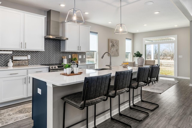 kitchen featuring pendant lighting, white cabinets, a center island with sink, and wall chimney range hood