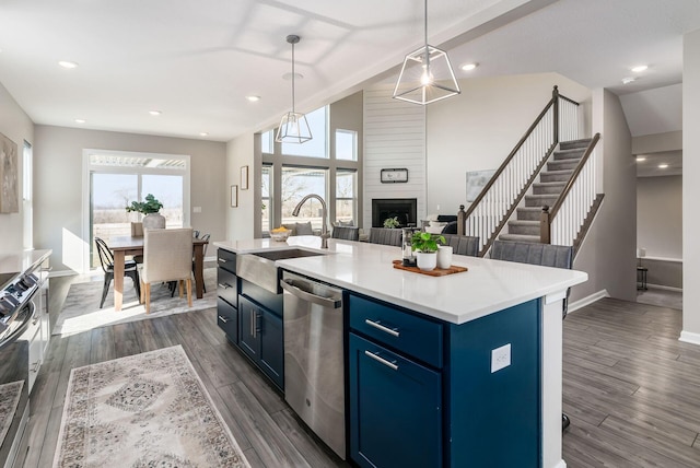 kitchen with light countertops, hanging light fixtures, stainless steel dishwasher, an island with sink, and blue cabinets