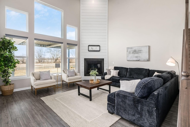 living area with a towering ceiling, a large fireplace, baseboards, and wood finished floors