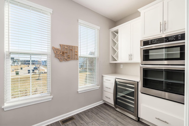 kitchen with wine cooler, stainless steel double oven, white cabinetry, light countertops, and open shelves