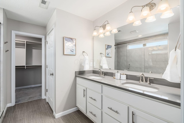 bathroom featuring double vanity, a stall shower, a spacious closet, and a sink