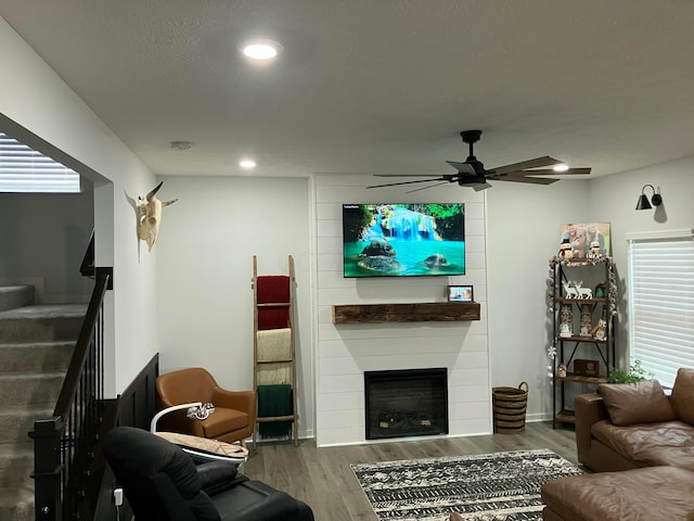 living area with a large fireplace, ceiling fan, stairway, dark wood-style flooring, and recessed lighting