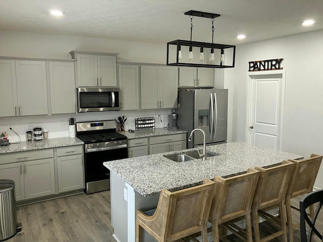 kitchen featuring stainless steel appliances, gray cabinetry, a kitchen island with sink, a sink, and a kitchen breakfast bar