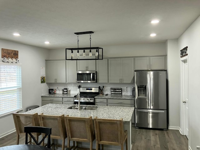 kitchen with light stone countertops, a center island with sink, appliances with stainless steel finishes, and gray cabinetry