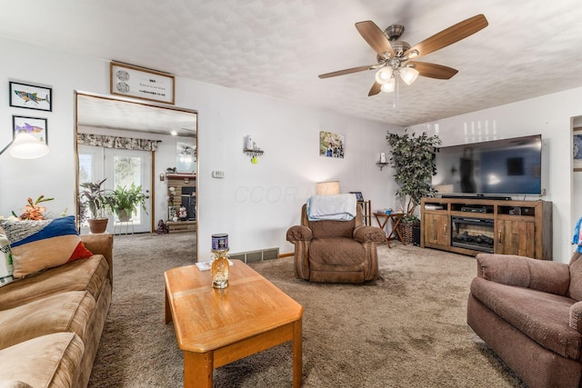 carpeted living room with a textured ceiling, visible vents, a ceiling fan, and a glass covered fireplace