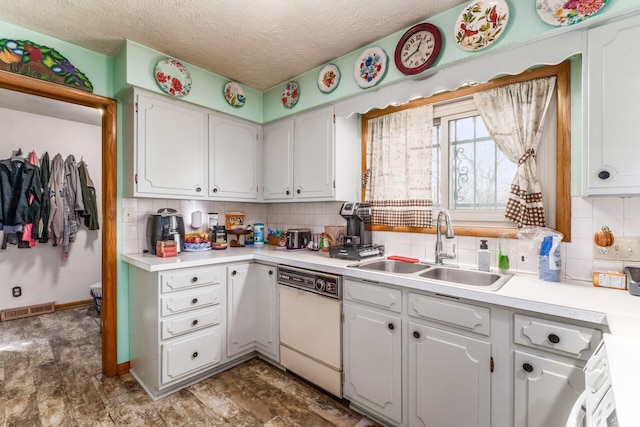 kitchen with light countertops, visible vents, white cabinetry, white dishwasher, and a sink