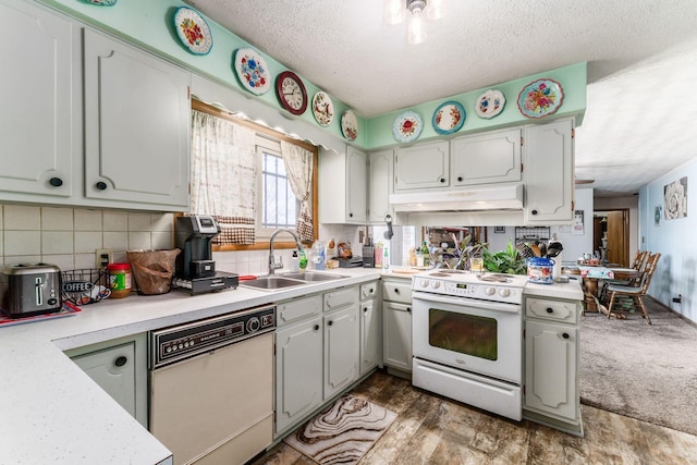 kitchen with under cabinet range hood, white appliances, a sink, light countertops, and decorative backsplash