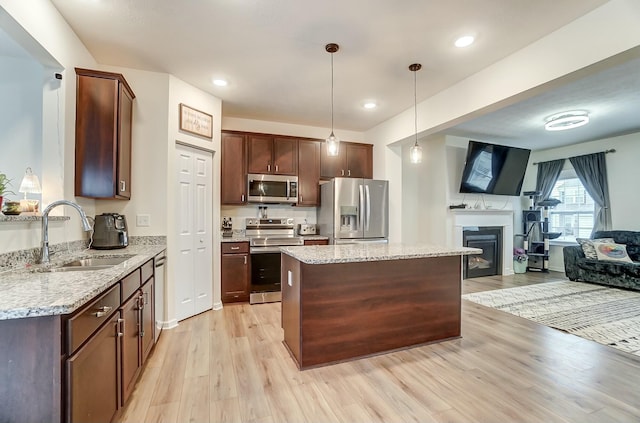 kitchen featuring light stone counters, hanging light fixtures, appliances with stainless steel finishes, open floor plan, and a sink