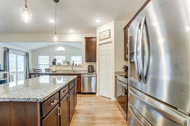 kitchen with light stone counters, light wood-style flooring, a kitchen island, hanging light fixtures, and appliances with stainless steel finishes