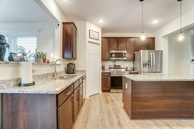 kitchen featuring stainless steel appliances, a sink, decorative light fixtures, and light stone countertops