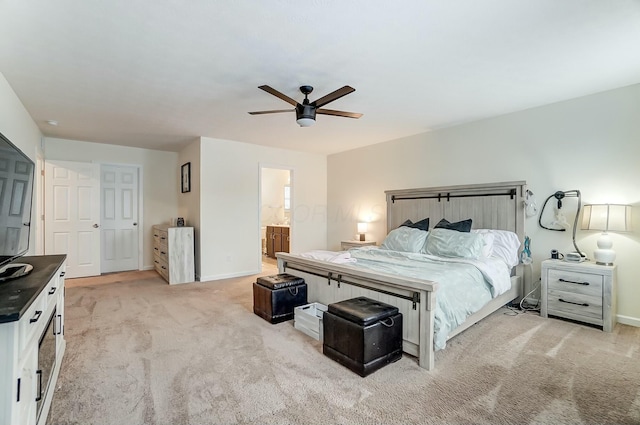 bedroom featuring light colored carpet, ceiling fan, baseboards, and ensuite bathroom