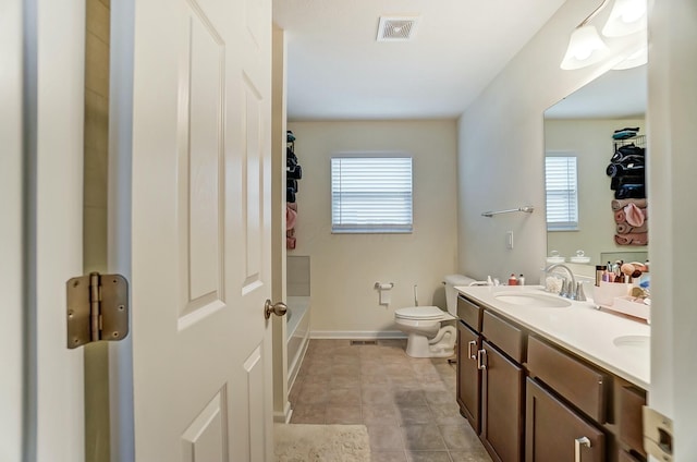 bathroom featuring double vanity, visible vents, toilet, a sink, and baseboards