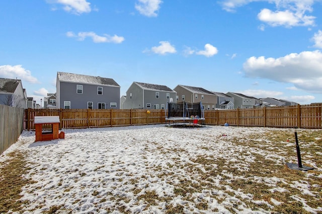 yard covered in snow with a trampoline, a fenced backyard, and a residential view