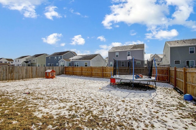 snowy yard featuring a trampoline, a residential view, and a fenced backyard