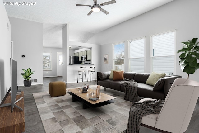 living area with a textured ceiling, wood finished floors, a ceiling fan, baseboards, and vaulted ceiling