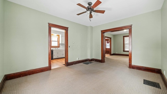 spare room featuring baseboards, visible vents, a ceiling fan, and light colored carpet