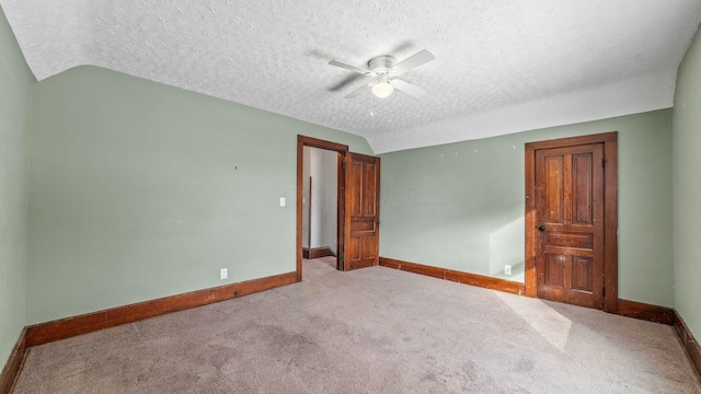 unfurnished room featuring lofted ceiling, light colored carpet, ceiling fan, a textured ceiling, and baseboards