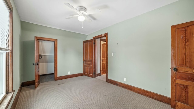 unfurnished bedroom with light carpet, ceiling fan, baseboards, and a walk in closet