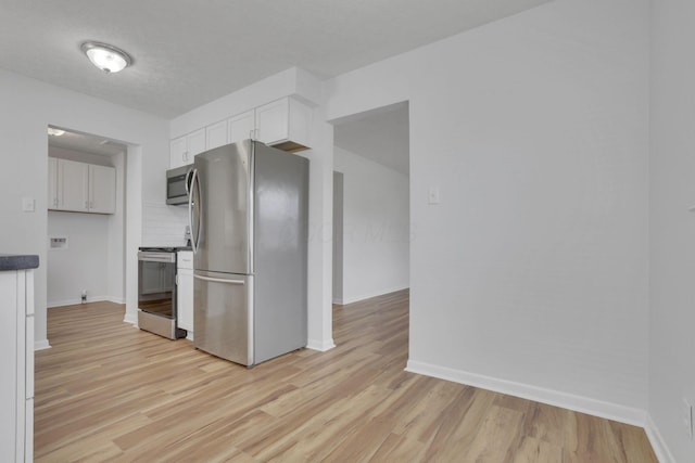 kitchen with stainless steel appliances, light wood-style flooring, white cabinetry, and baseboards