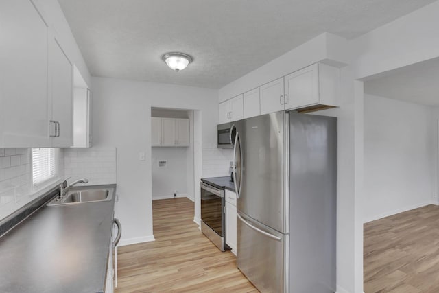 kitchen with appliances with stainless steel finishes, dark countertops, a sink, and white cabinets