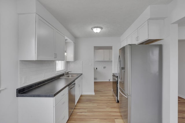 kitchen featuring stainless steel appliances, dark countertops, a sink, and white cabinets