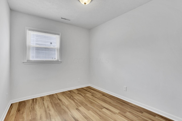 spare room featuring light wood-type flooring, visible vents, a textured ceiling, and baseboards