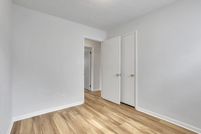 spare room featuring baseboards, a textured ceiling, and light wood finished floors