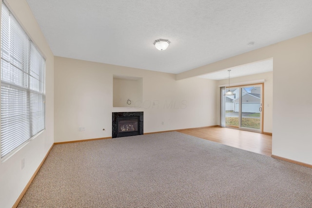 unfurnished living room with a textured ceiling, carpet, a high end fireplace, and baseboards