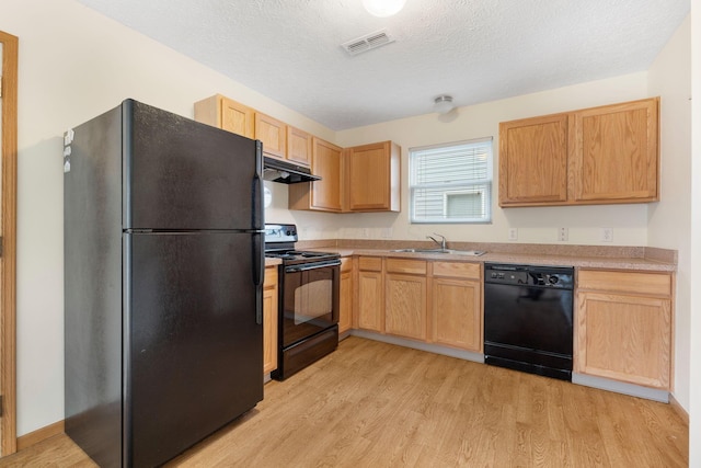 kitchen with visible vents, a sink, light wood-type flooring, under cabinet range hood, and black appliances