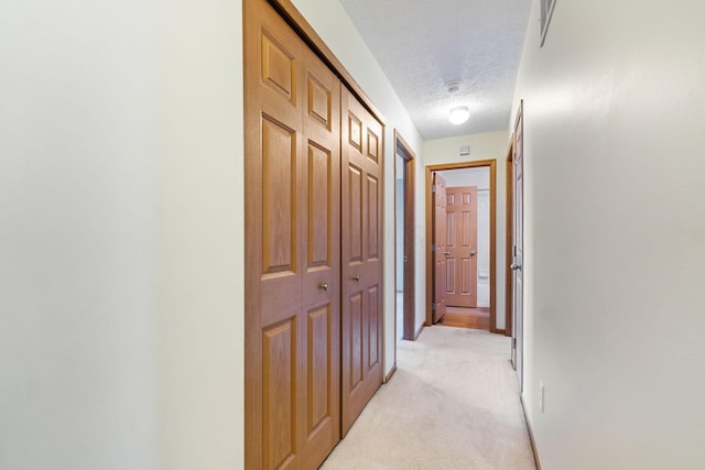 hallway with visible vents, light carpet, a textured ceiling, and baseboards