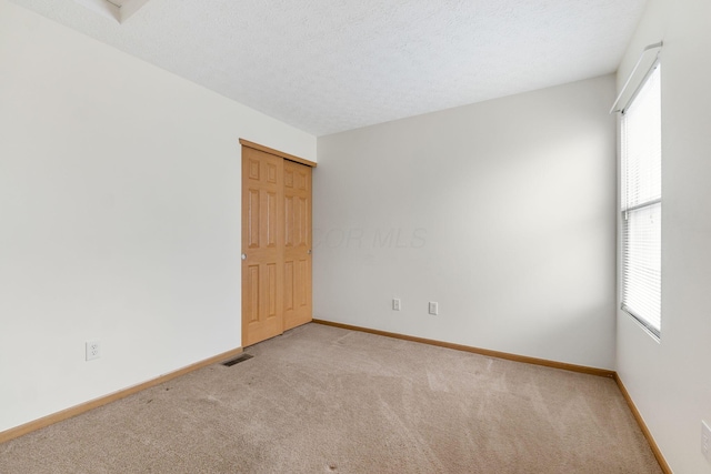 spare room featuring a wealth of natural light, visible vents, light carpet, and a textured ceiling