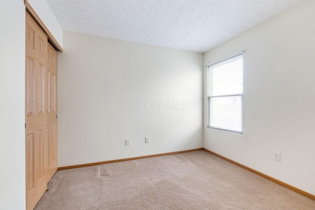 unfurnished bedroom with light carpet, a textured ceiling, a closet, and baseboards