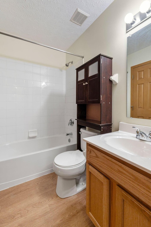 full bath featuring visible vents, toilet, vanity, a textured ceiling, and wood finished floors