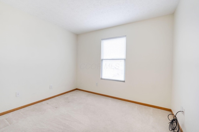 spare room with light carpet, a textured ceiling, and baseboards