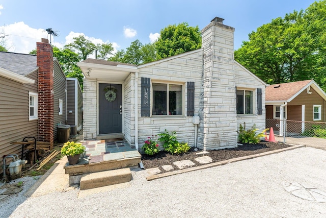 view of front of house featuring stone siding, a chimney, and fence