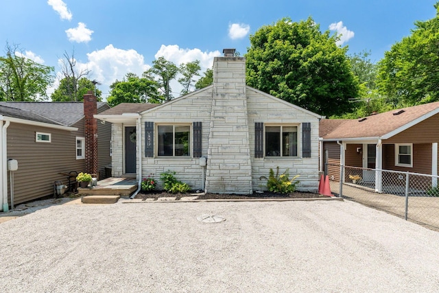 bungalow-style home with stone siding, a chimney, and fence